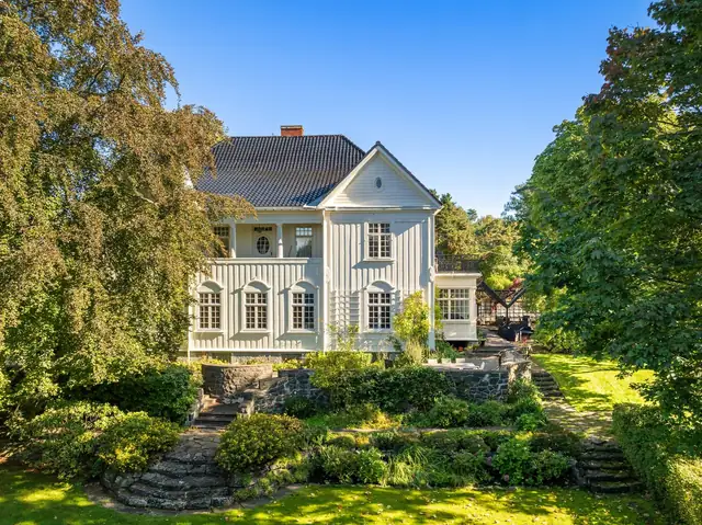 Den vakre villaen ligger flott til på tomtens høyeste punkt, og fasaden har original kledning med markante og noe dekorerte hjørnekasser.