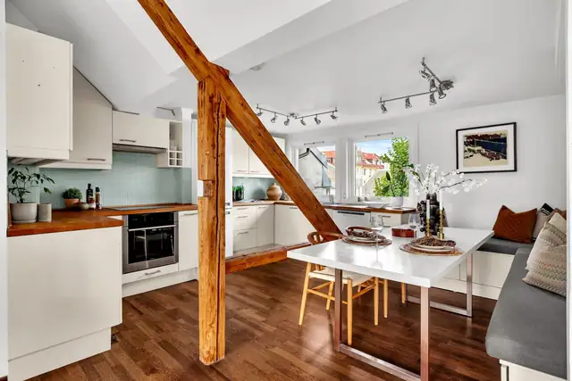 Stilrent kjøkken med innredning bestående av over- og underskap med glatte fronter, benkeplate i eik, og glassmosaikkfliser på vegg over benk.