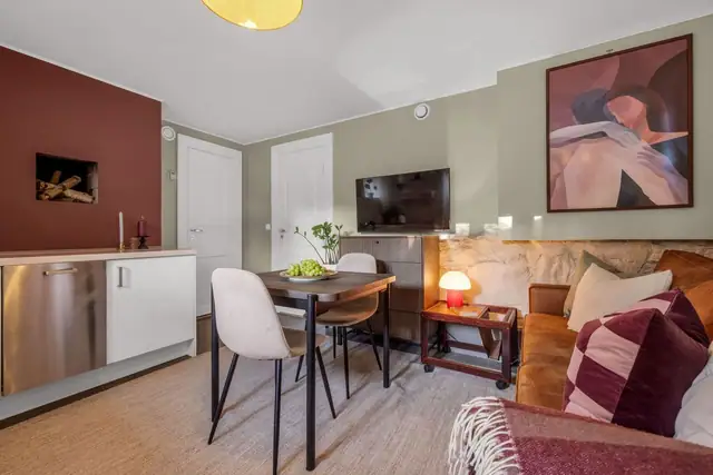 Rommet har åpen løsning til stuen med plass til sofaseksjon, lite spisebord og tv-møblement.