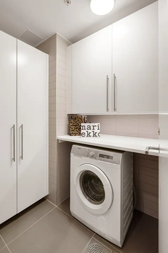 I likhet med badet har vaskerommet sandfargede fliser på vegger og gulv, og av spesialtilpasset innredning er det hvite overskap, hvite høyskap og hvit benkeplate. Her er det også plass til tørketrommel.