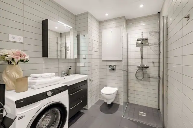 Badet er romslig og funksjonelt innredet med et tidløst materialvalg og gode løsninger for hverdagen. Grå gulvfliser kombineres med lyse veggfliser, mens downlights i himlingen sørger for god og behagelig belysning.